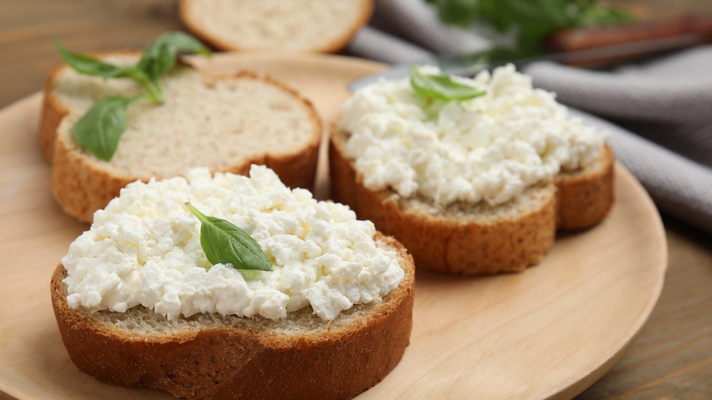 Brot mit Hüttenkäse Vollkornbrote mit Hüttenkäse auf einem Holzuntergrund und verziert mit Basilikum.