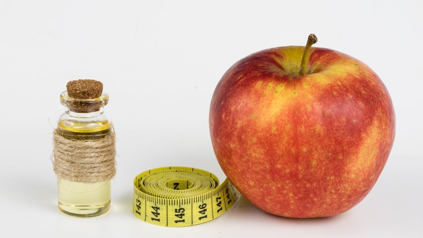 Ein Apfel, ein kleines Fläschchen Apfelessig und ein gelbes gerollte Maßband