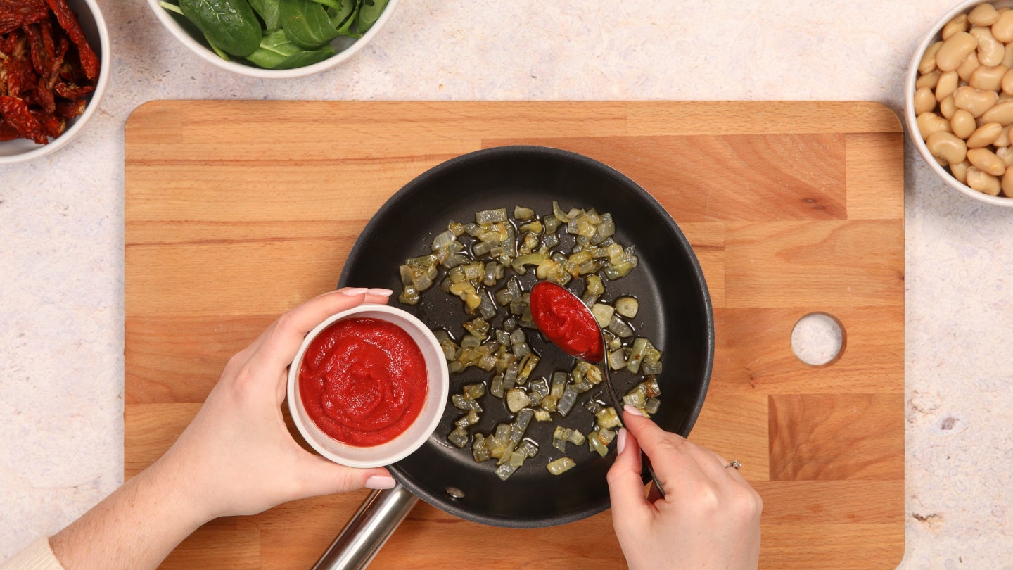Tomatenpaste wird in die Pfanne hinzugegeben