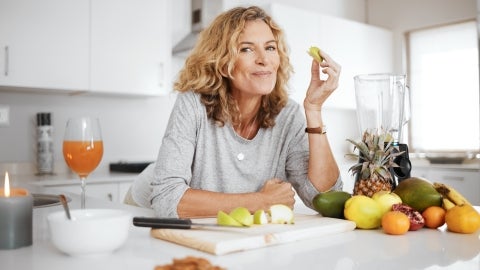 Eine Frau in der Küche, die mit einem Lächeln frisches Obst isst