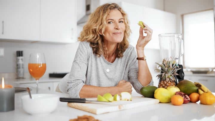 Eine Frau in der Küche, die mit einem Lächeln frisches Obst isst