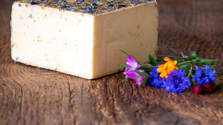 Ein Stück Bergkäse beschmückt mit ein paar Blumen in Lila, Blau, Gelb und Rot