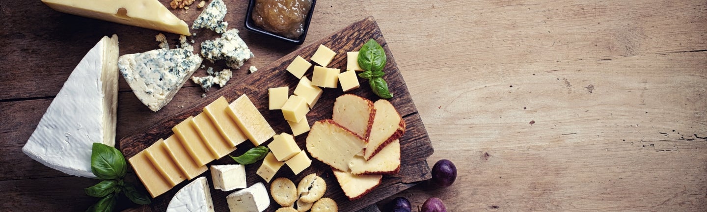 Fettarmer Käse: Ansprechende Käseplatte, verschiedene Käsesorten auf Holzbrett, verziert mit Trauben und Feigen.