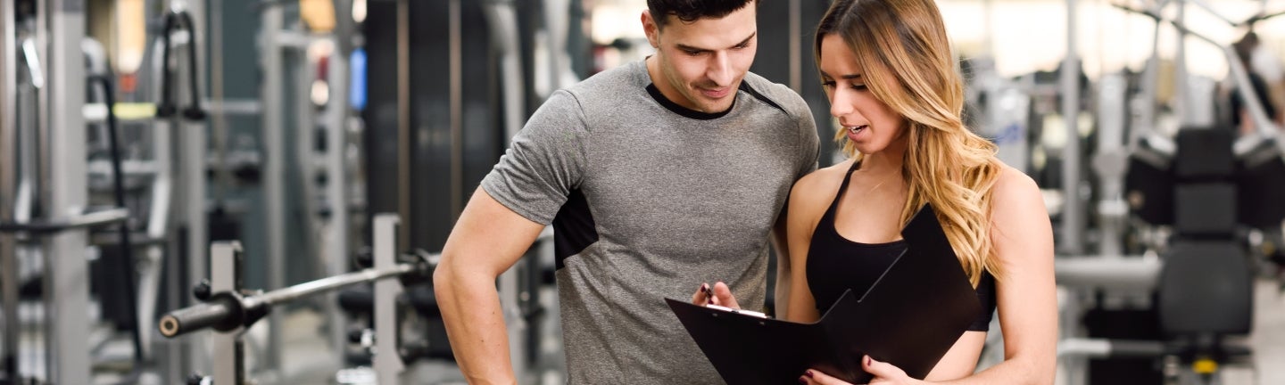 Frau im Fitnessstudio zeigt einem Mann den Trainingsplan.