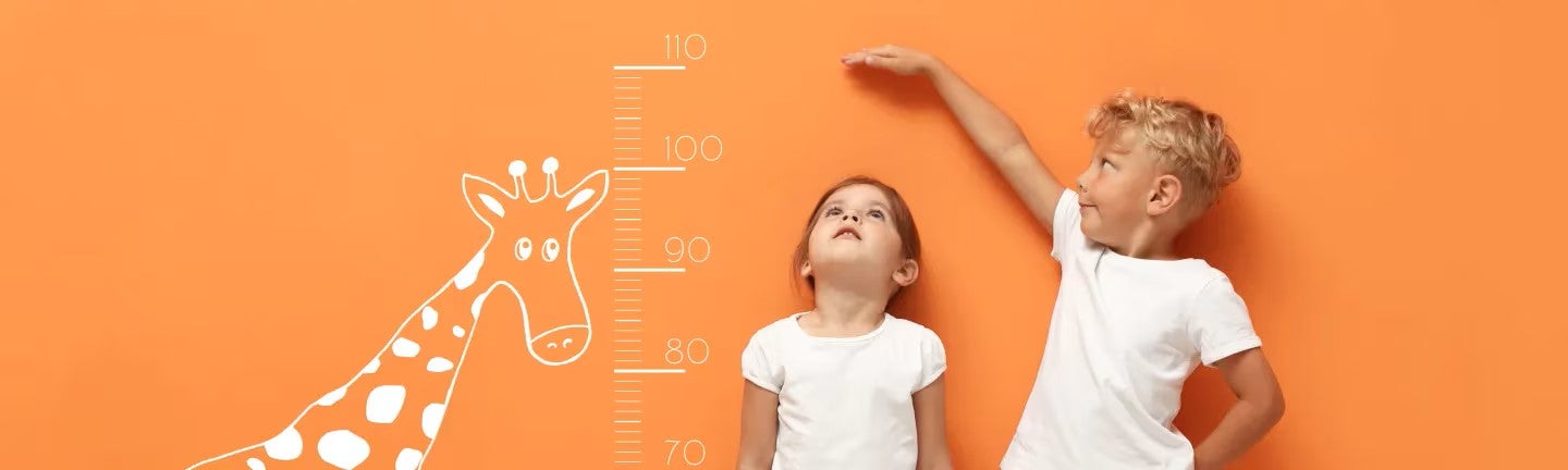 Zwei Kinder stehen vor einer Wand, messen sich