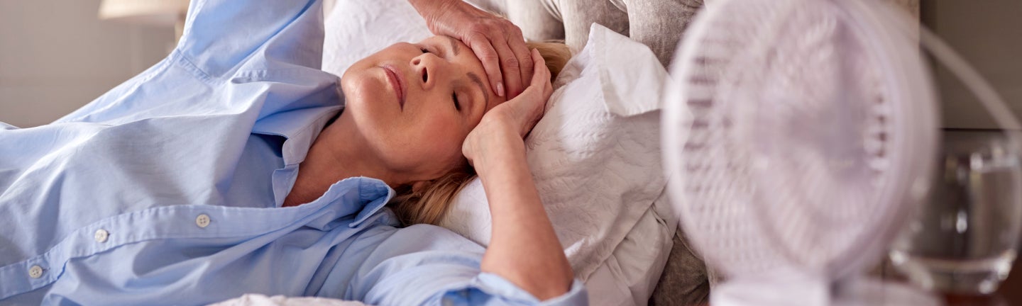 Frau liegt erschöpft im Bett, mit ihrer Hand auf der Stirn