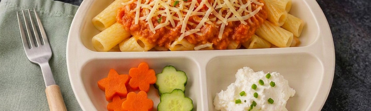 Ein angerichteter  Teller Nudeln mit Tomatensoße, sowie Frischkäse und etwas Gemüse